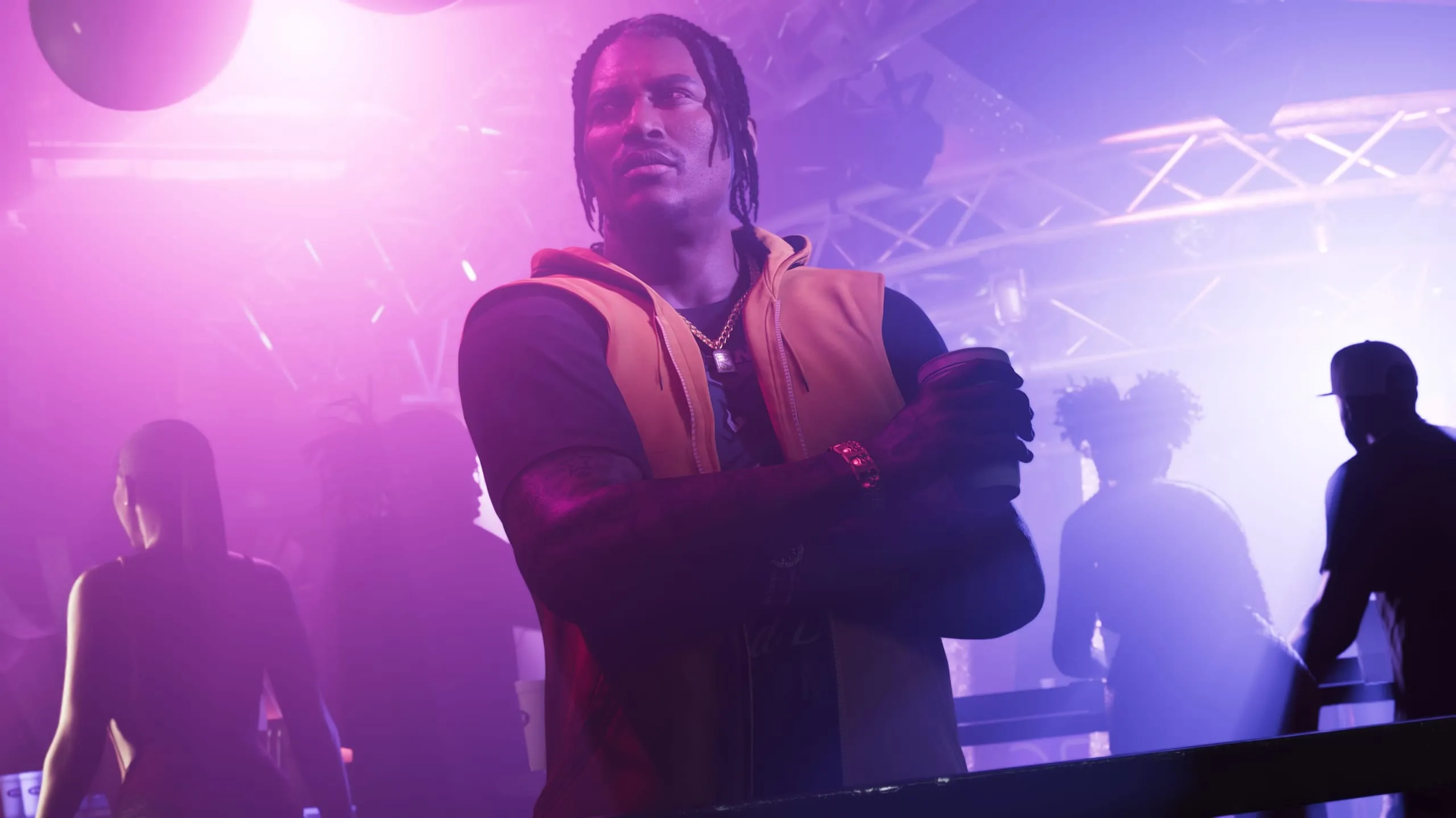 Man in an orange vest folds his arms, cup in hand, in a smoky purple club