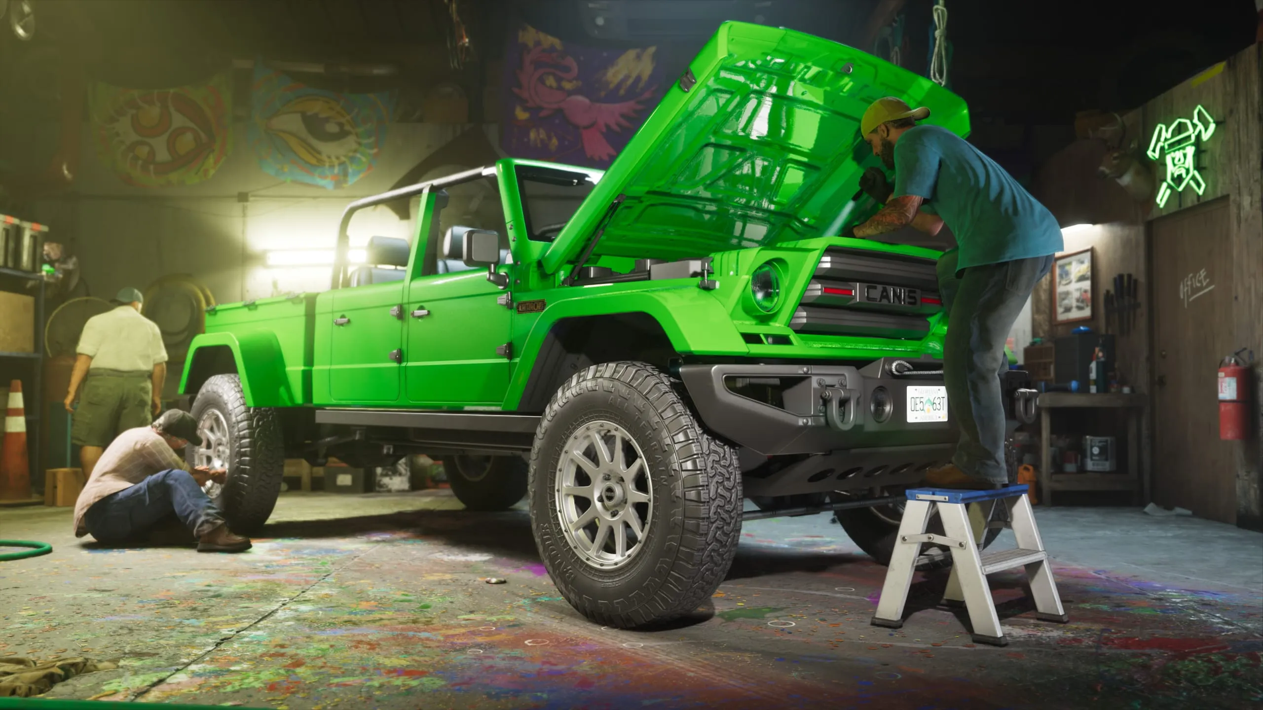 Two men working on a green 4x4 with the hood up in a paint-spattered workshop