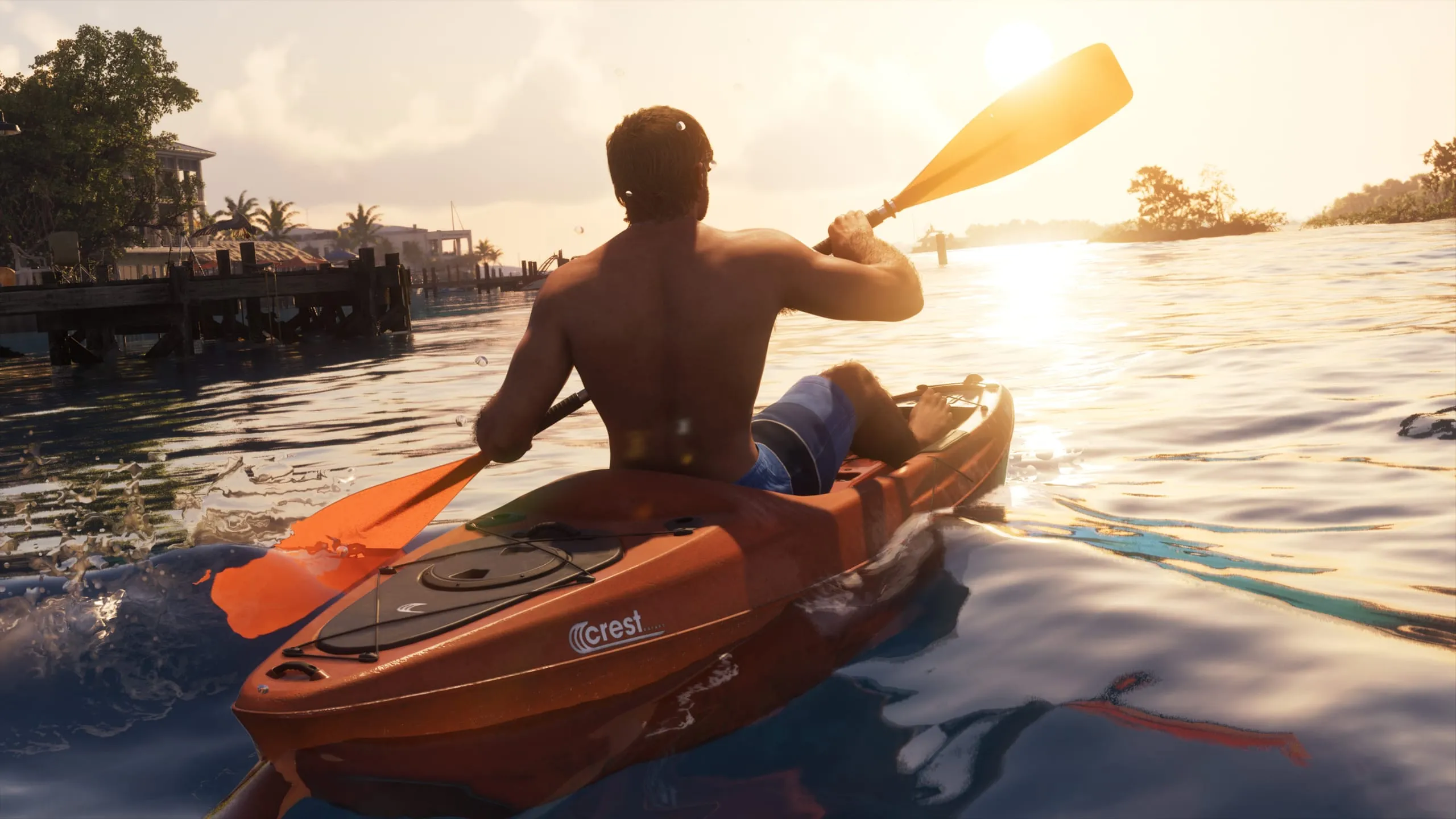 Shirtless man paddling an orange kayak at sunset, a second person lying on the bow